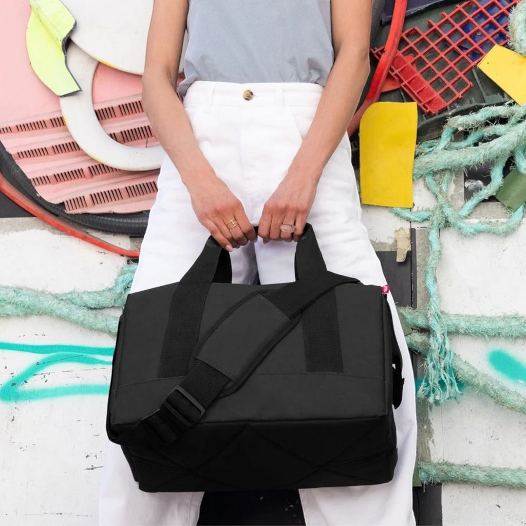 Lieblingstasche Allrounder M black travel bag with padded shoulder strap and metal frame closure held by a person.