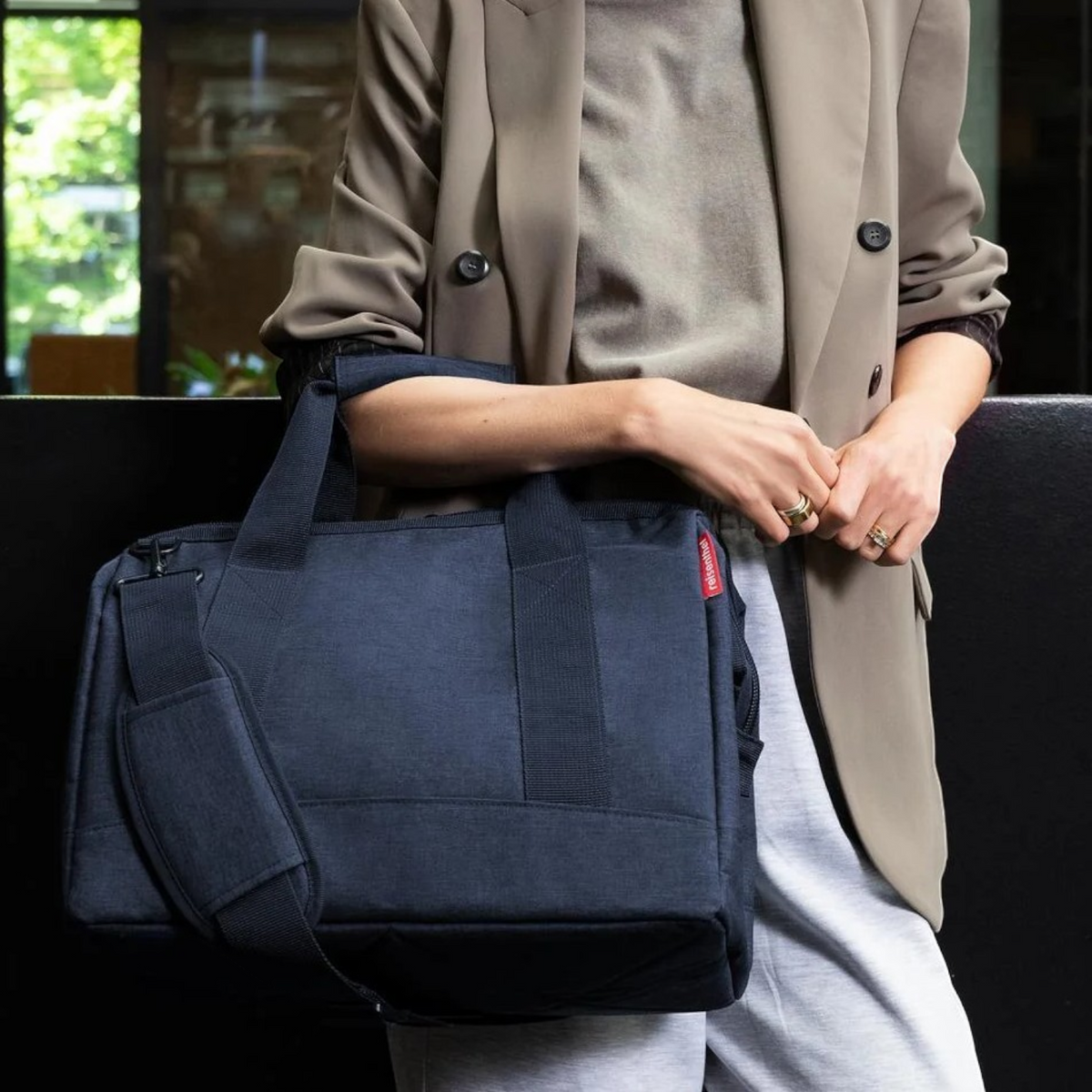 Lieblingstasche Allrounder M navy blue travel bag with shoulder strap carried by a woman in a beige blazer