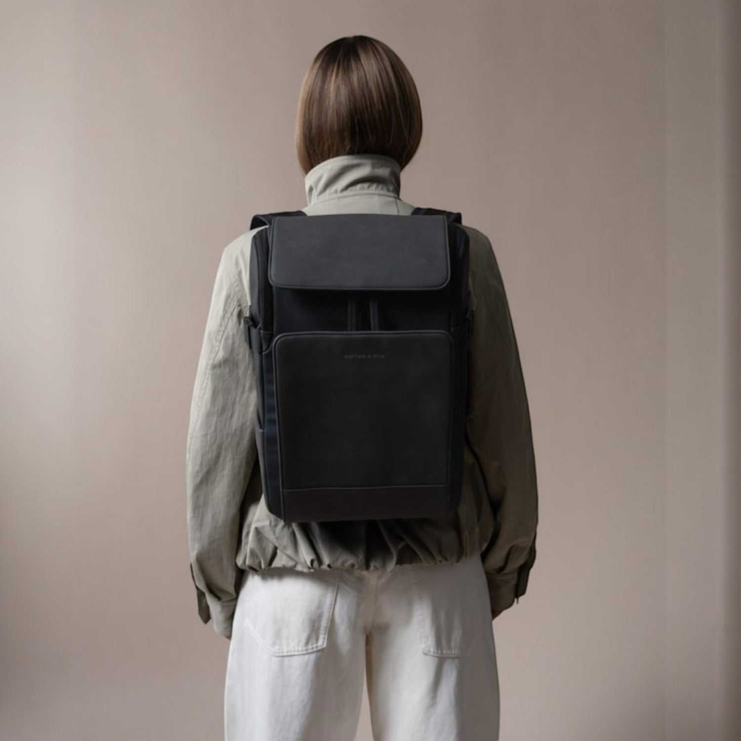 Lieblingstasche Bali Pro black backpack with flap closure and front pocket, worn by a person with light-colored pants and a green jacket.