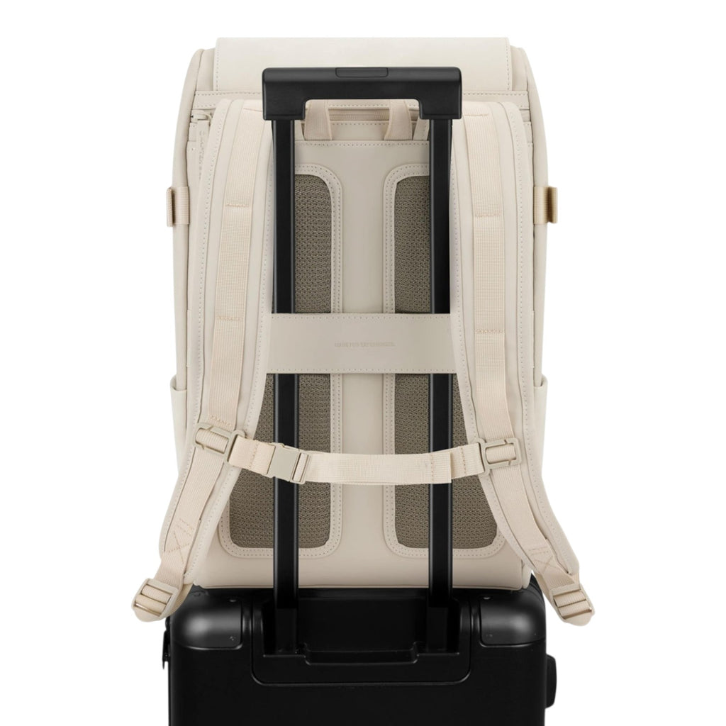 Lieblingstasche Bali Pro cream vegan leather backpack with padded straps and luggage sleeve, attached to a black suitcase.