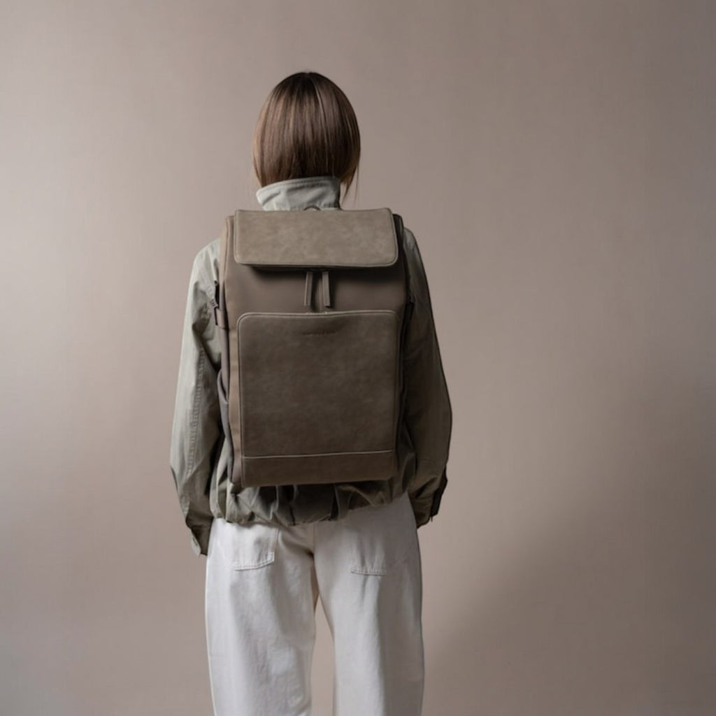 Lieblingstasche Bali Pro taupe faux leather backpack with flap closure and front pocket, worn by a person from behind.