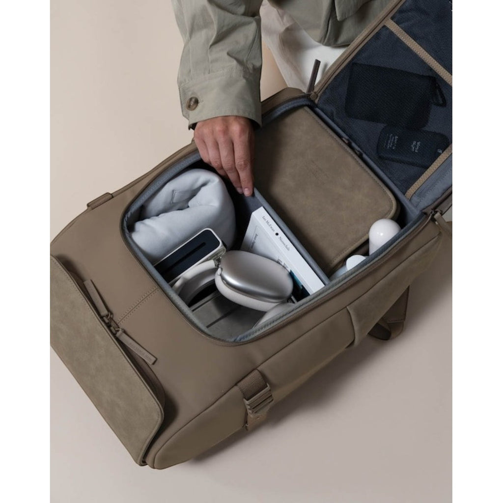 Lieblingstasche Bali Pro taupe backpack with organized compartments holding a book, headphones, and travel pillow.