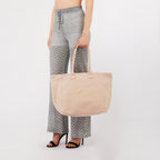 Lieblingstasche Tote L in beige canvas with embroidered logo, held by a woman wearing chevron patterned trousers.