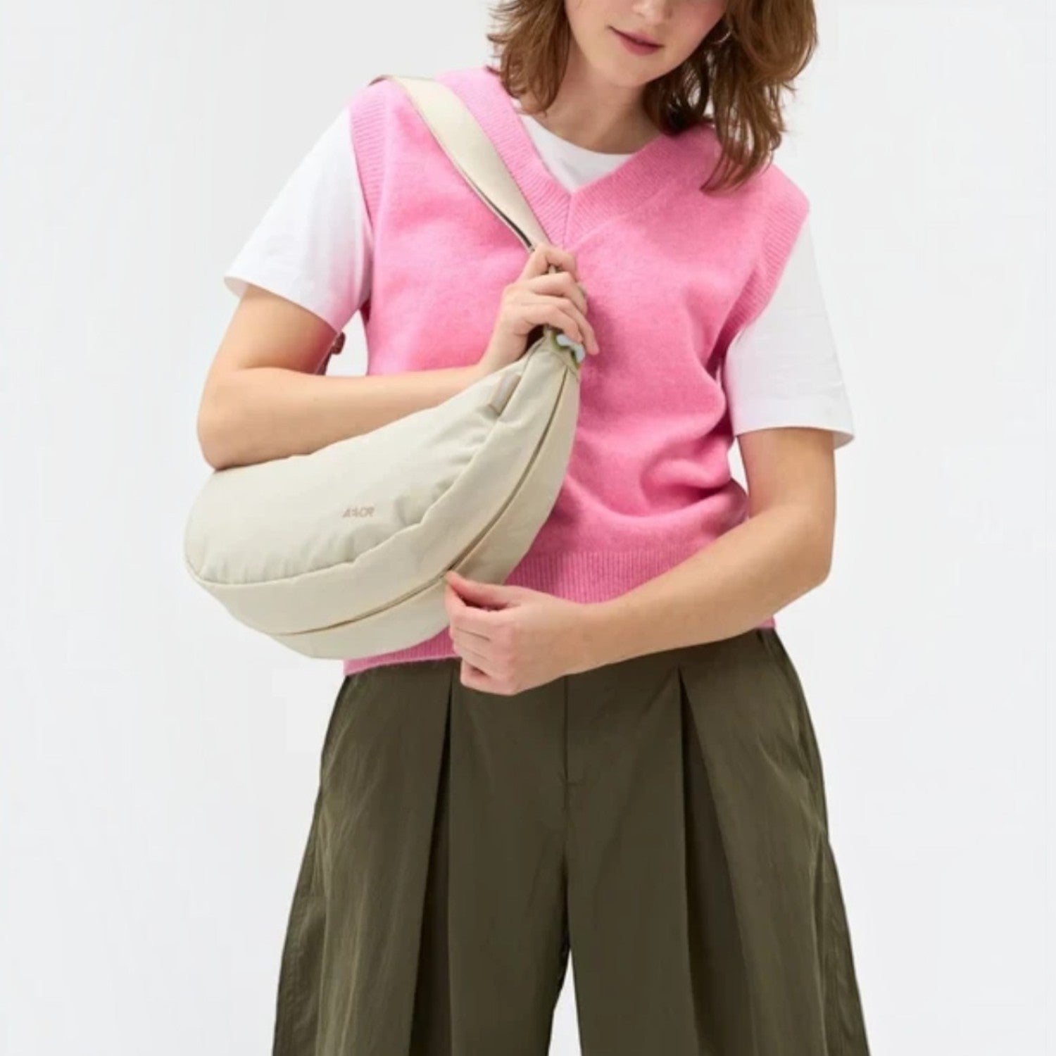 Lieblingstasche beige water-resistant sling bag worn crossbody by a woman in a pink vest for urban travel