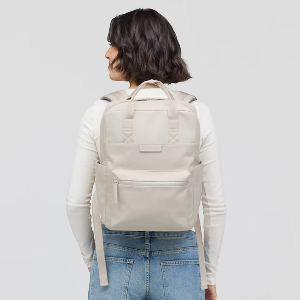 Woman wearing a beige Lieblingstasche Bergen Pro backpack with padded straps and front pocket, back view