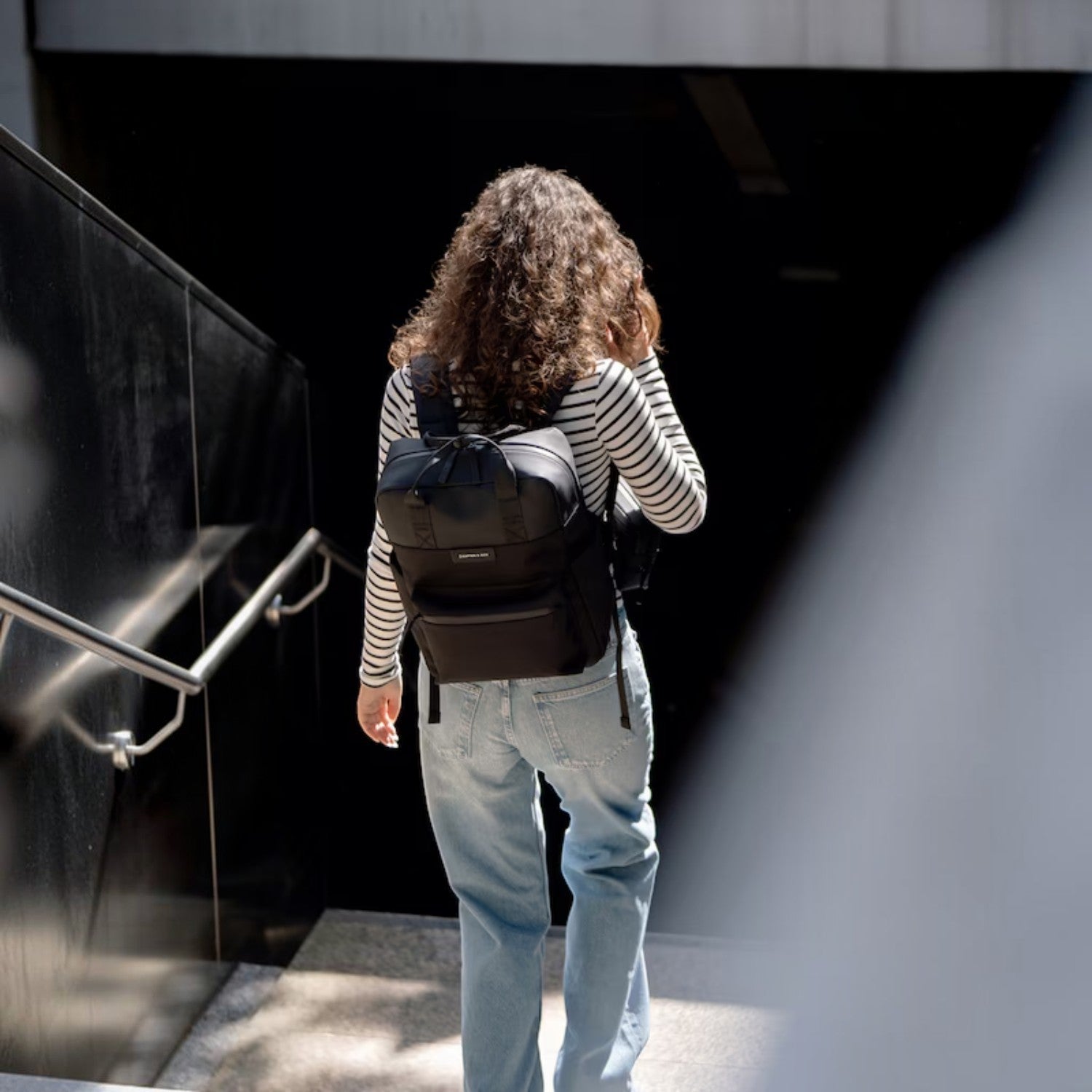 Lieblingstasche Bergen Pro black laptop backpack worn by a woman with curly hair in a striped shirt and jeans