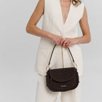 Lieblingstasche Big Sister Suede dark brown shoulder bag held by a woman in a cream-colored vest and trousers