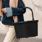 Lieblingstasche Carrybag in black with a sturdy aluminium handle, held by a person wearing a denim jacket.