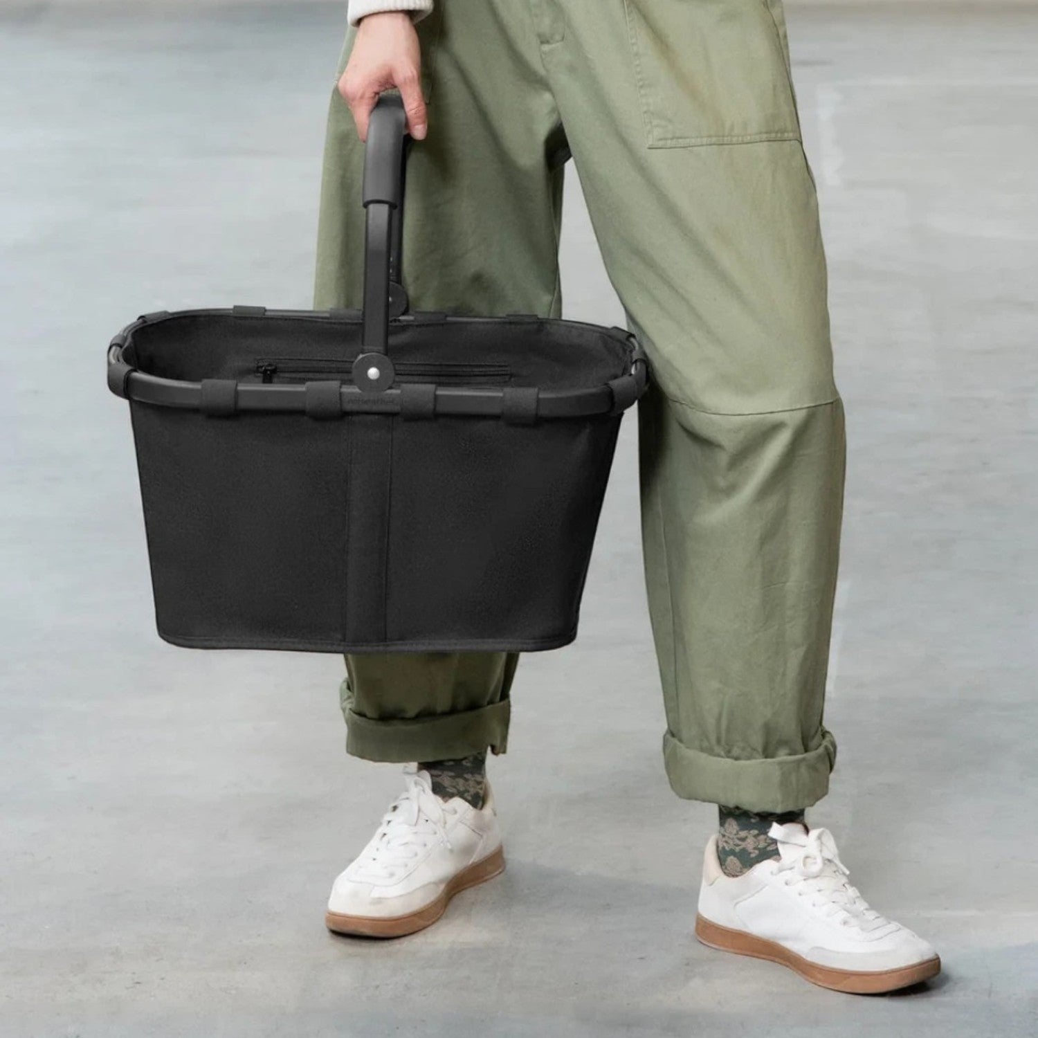 Lieblingstasche carrybag in black with a sturdy aluminium handle, held by a person in casual urban clothing.