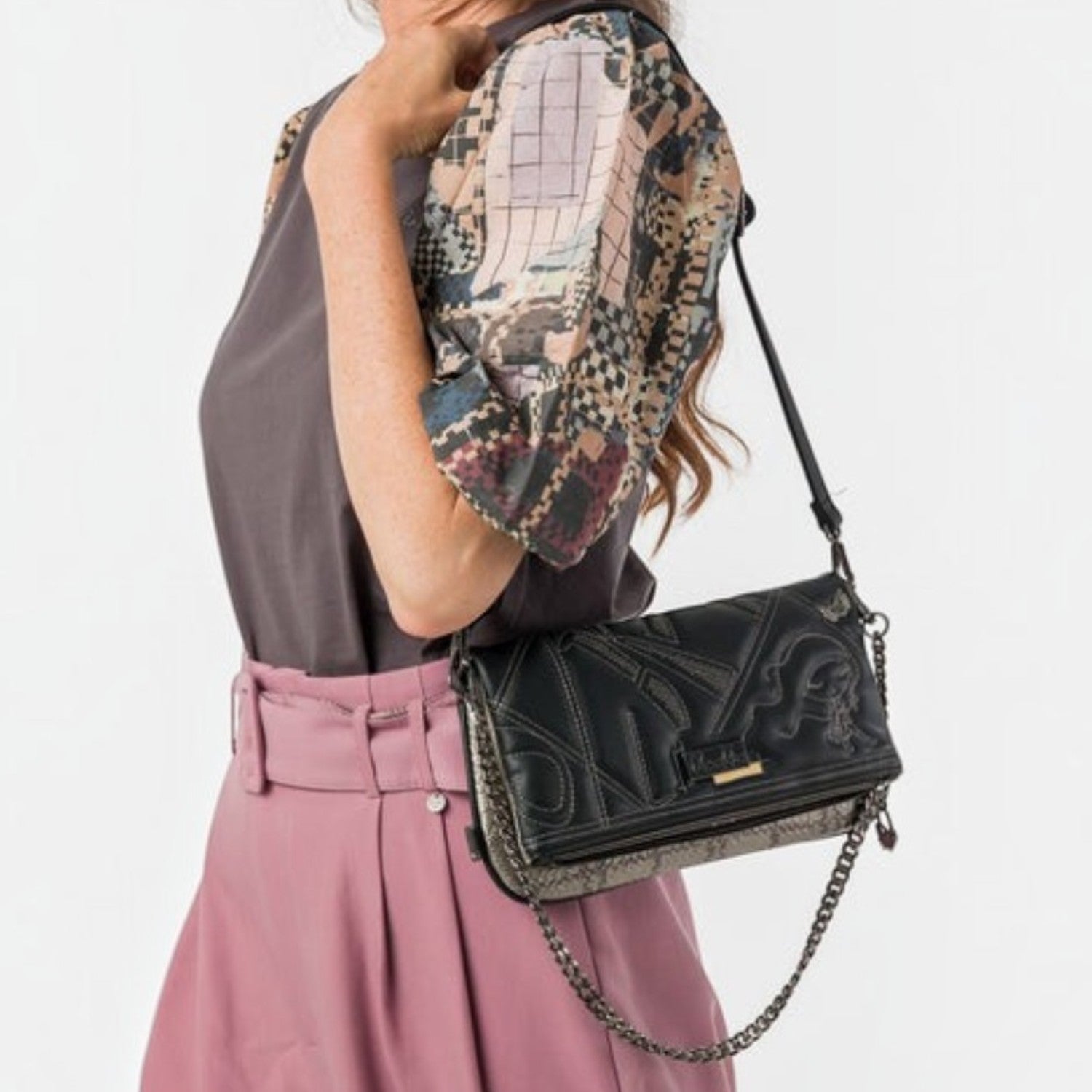 Lieblingstasche black cross-body bag with embossed geometric patterns and a dark metal chain strap worn by a woman