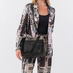 Lieblingstasche black shoulder bag with embossed pattern and metallic hardware worn by a model in a patterned suit