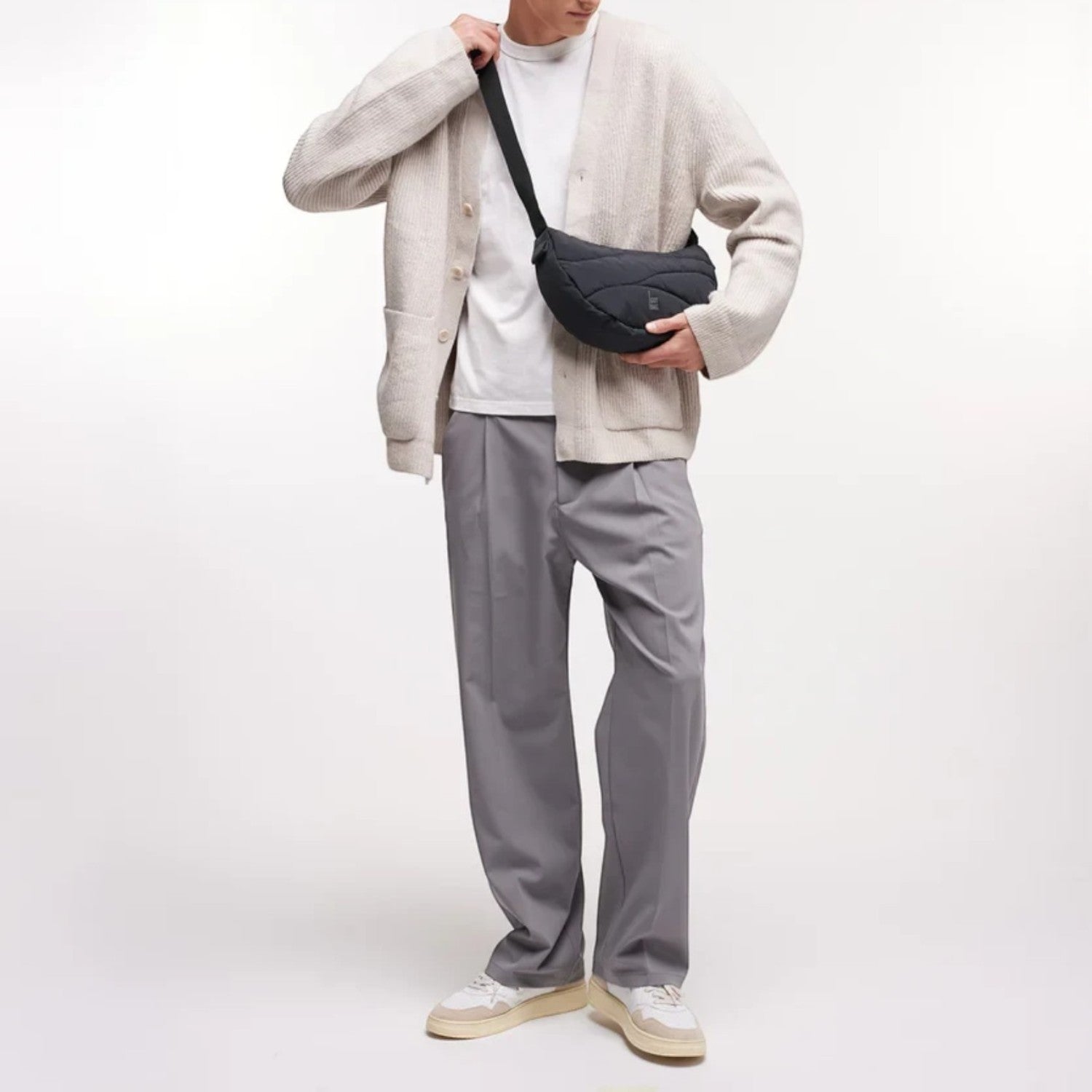 Lieblingstasche black wavy puffer moon bag worn crossbody by a man in a beige cardigan and grey trousers