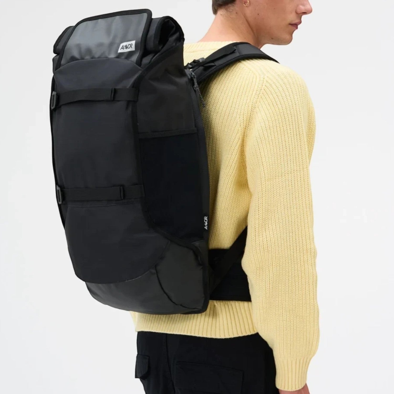 Lieblingstasche Travel Pack black rolltop backpack with adjustable straps worn by a man in a yellow sweater