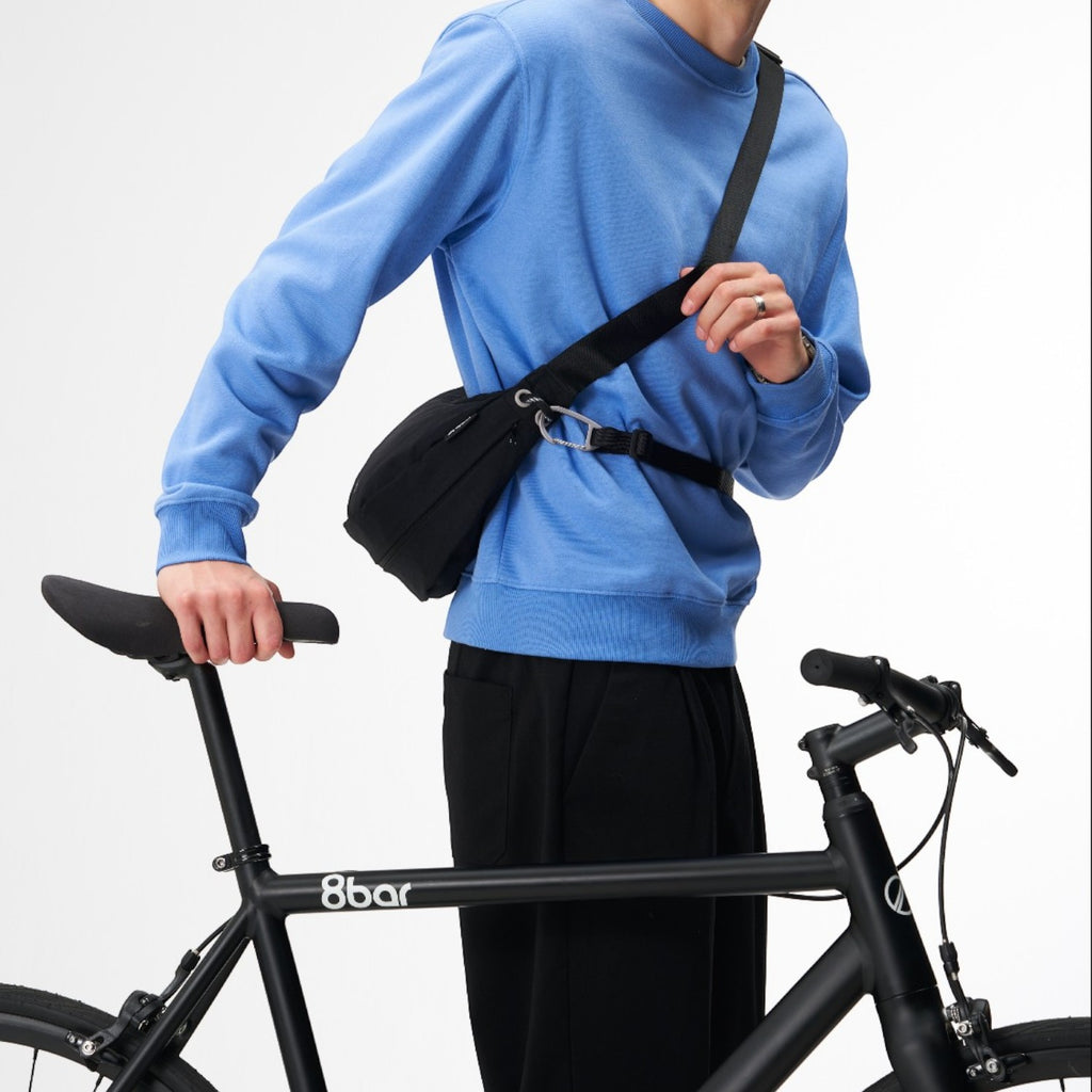 Lieblingstasche black sling bag worn across the chest by a man in a blue sweatshirt holding a bicycle