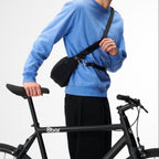 Lieblingstasche black sling bag worn across the chest by a man in a blue sweatshirt holding a bicycle