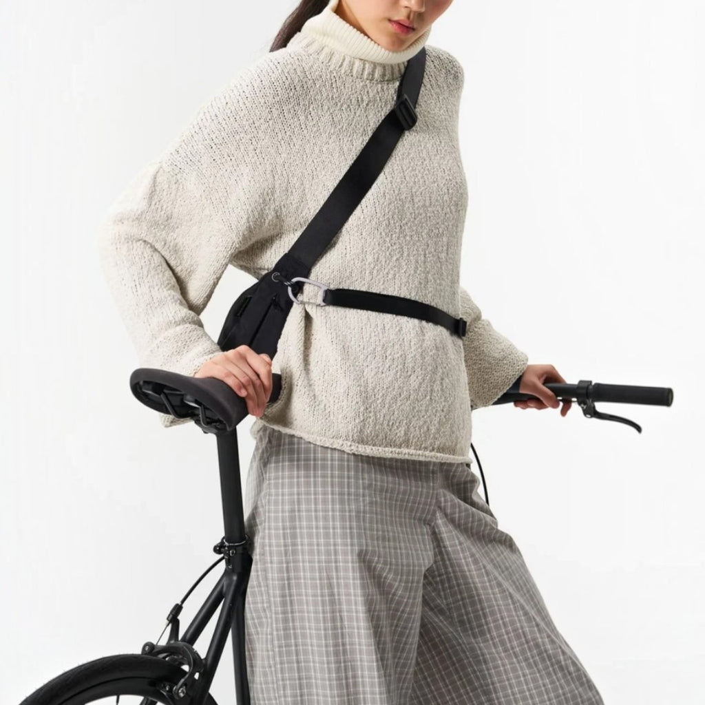 Lieblingstasche black water-resistant sling bag worn crossbody by a cyclist in a beige sweater