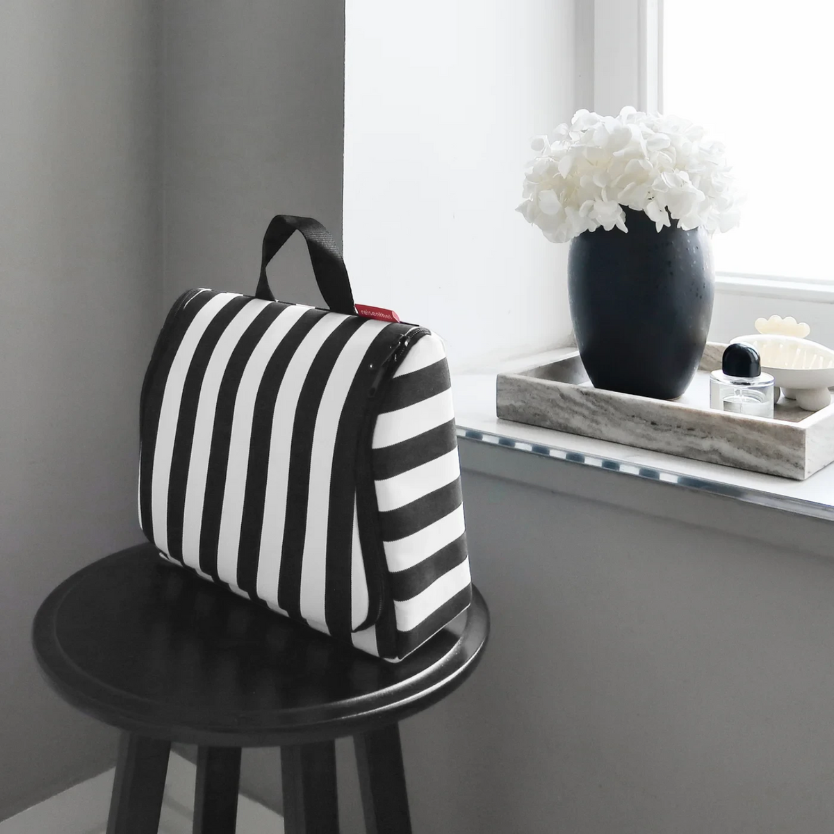 Lieblingstasche Toiletbag XL featuring a black and white striped pattern, displayed on a small black stool.