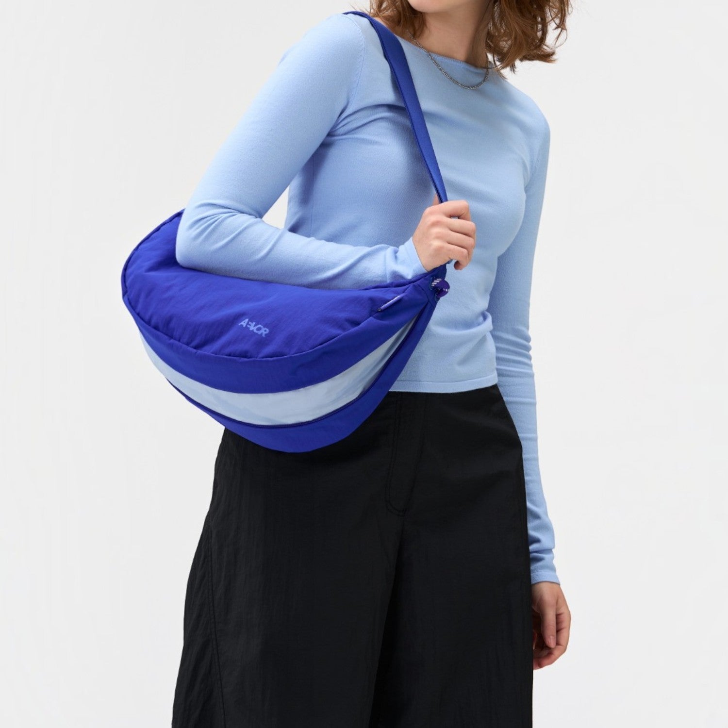 A woman wearing a Lieblingstasche blue crescent-shaped sling bag with a light blue accent stripe over her shoulder.