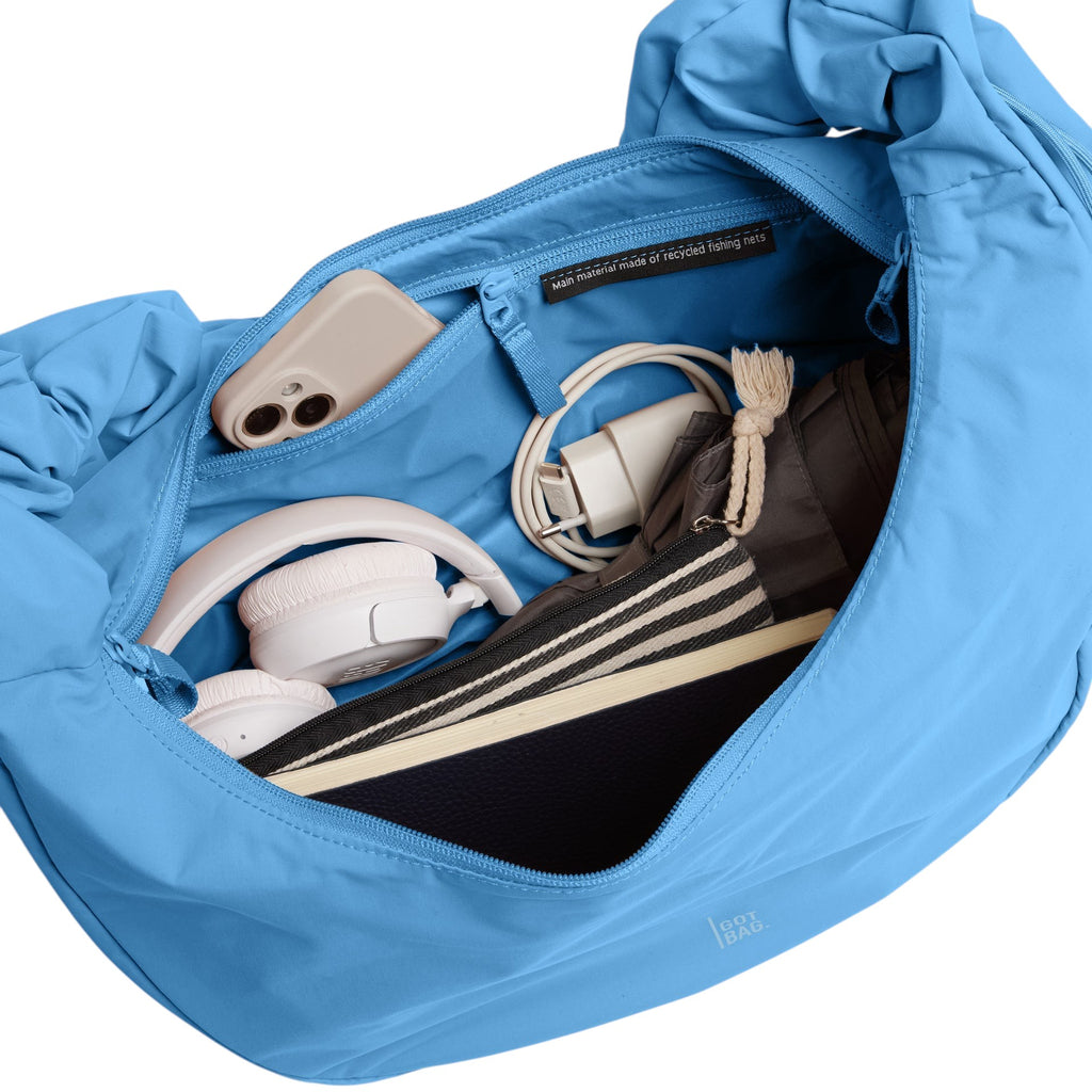Lieblingstasche large blue moon bag with ruffled details, open to show contents: phone, headphones, charger, and book.