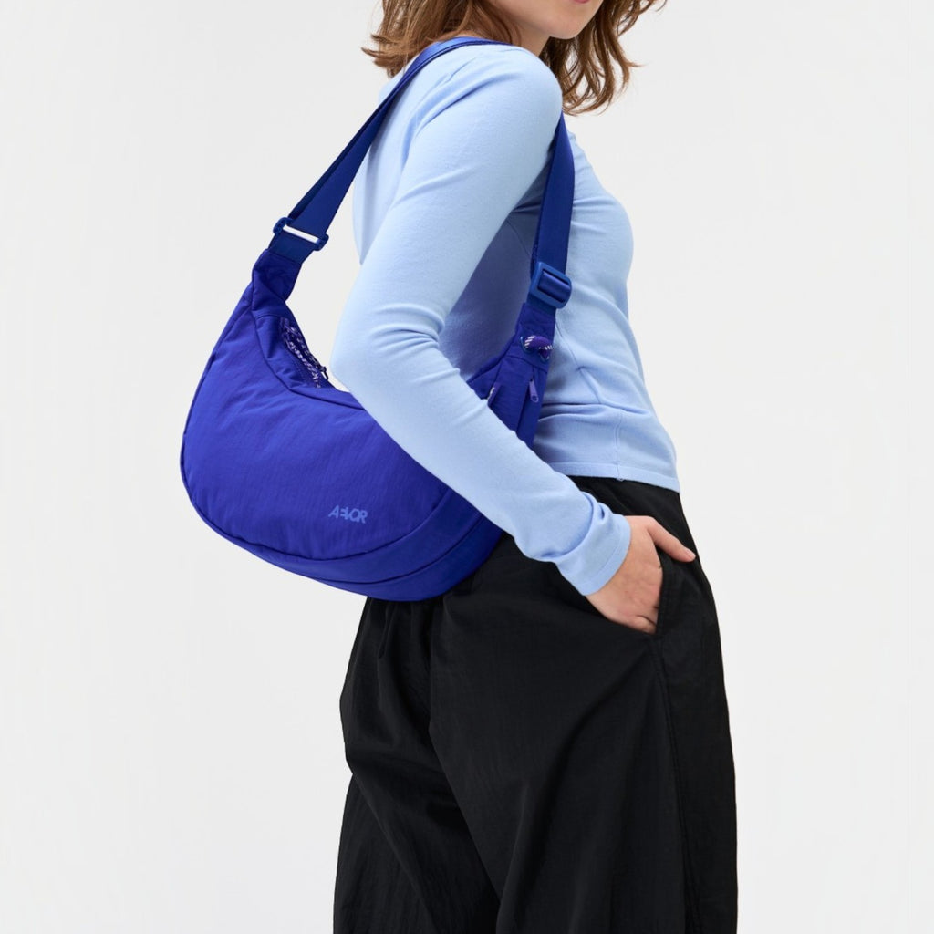 A model wearing a vibrant blue Lieblingstasche sling bag with an adjustable strap against a plain white background.