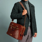 Lieblingstasche brown leather briefcase with gold hardware, worn by a man in a grey coat and turtleneck.