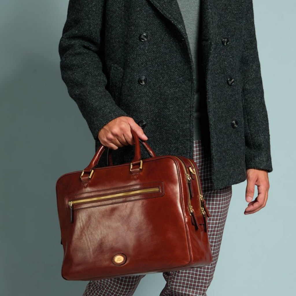 Lieblingstasche brown leather briefcase with gold hardware, held by a man in a grey turtleneck and charcoal coat.