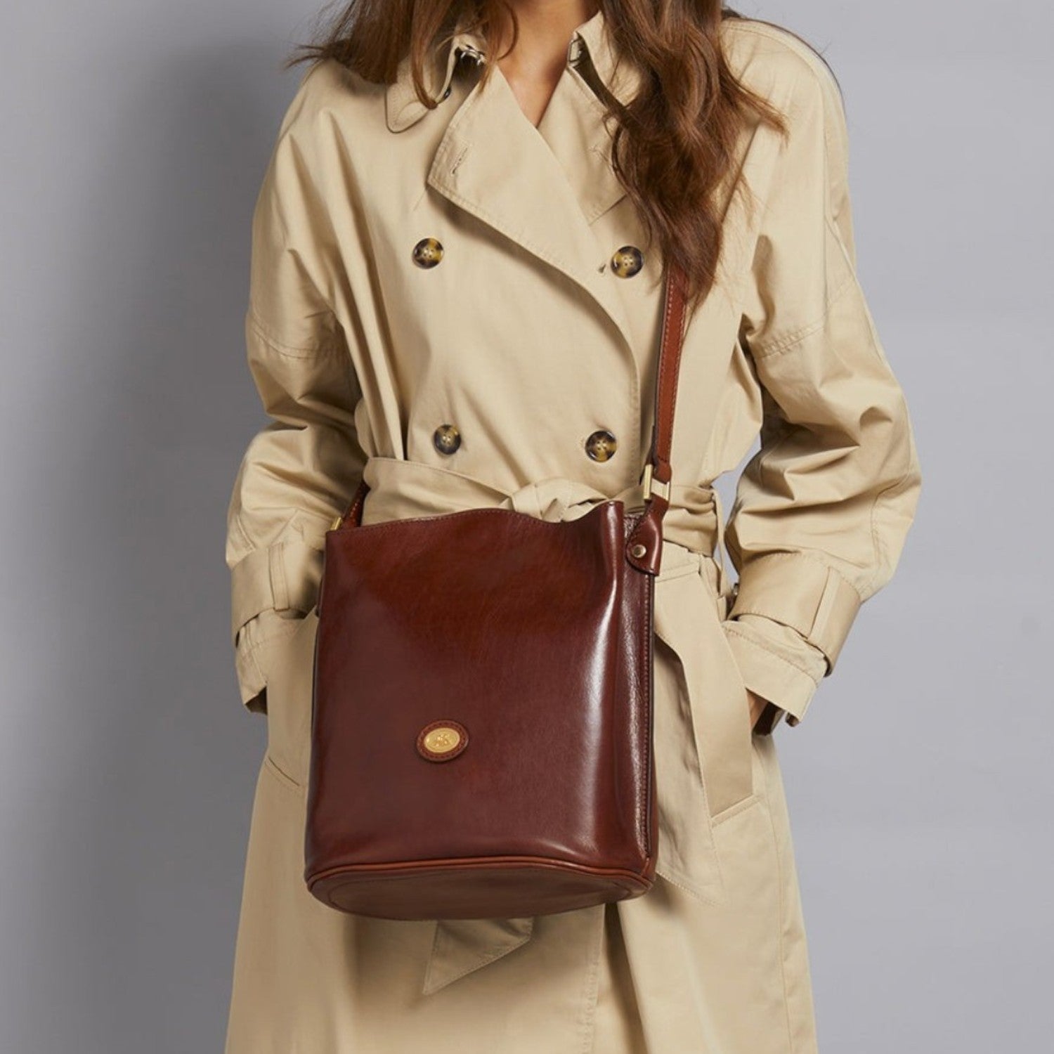 Lieblingstasche brown leather bucket bag with gold emblem worn by a model in a beige trench coat.