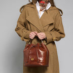 Lieblingstasche brown leather drawstring bucket bag with shoulder strap, worn by a model in a tan coat.