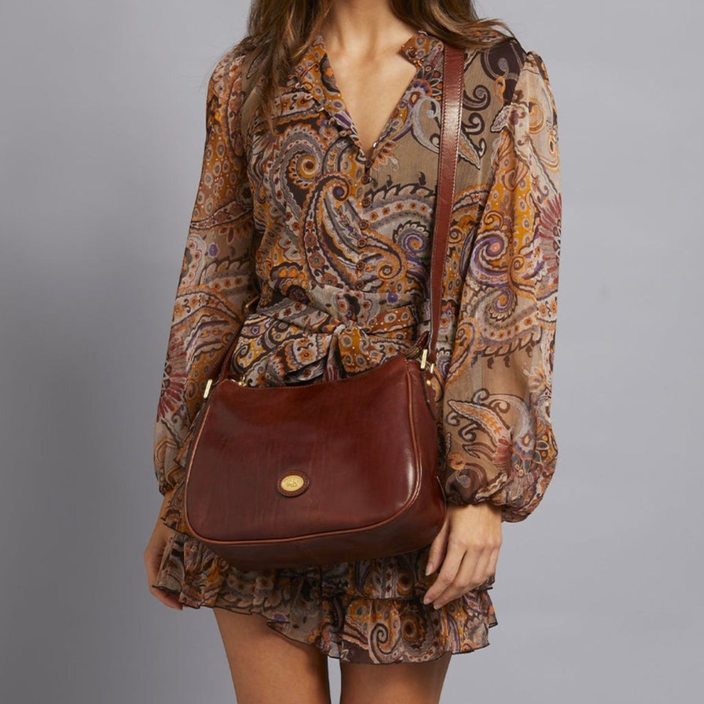 Lieblingstasche brown leather shoulder bag with zipper closure and gold hardware, worn by a model in a paisley print dress.