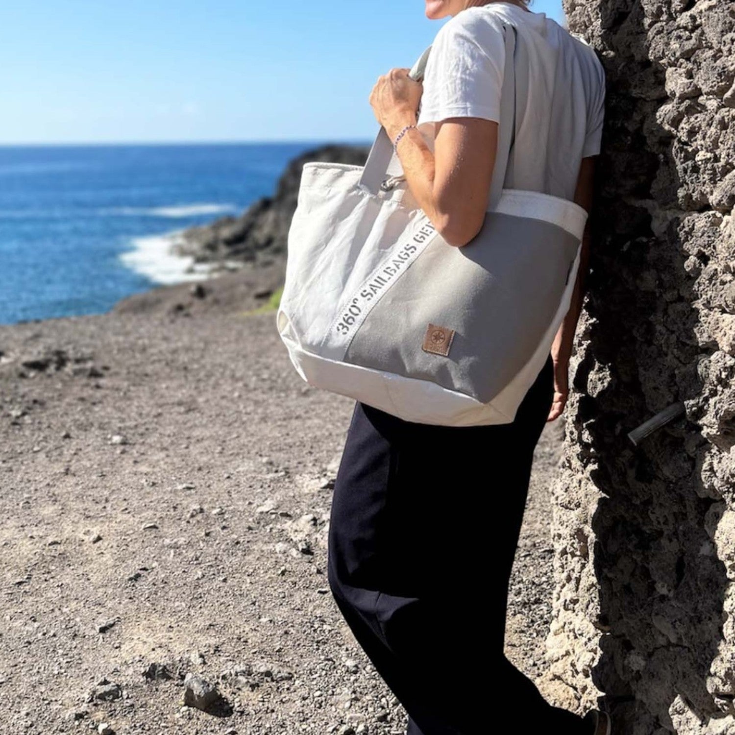 Lieblingstasche canvas tote bag in cream and grey with text detail, worn by a woman outdoors by the sea.