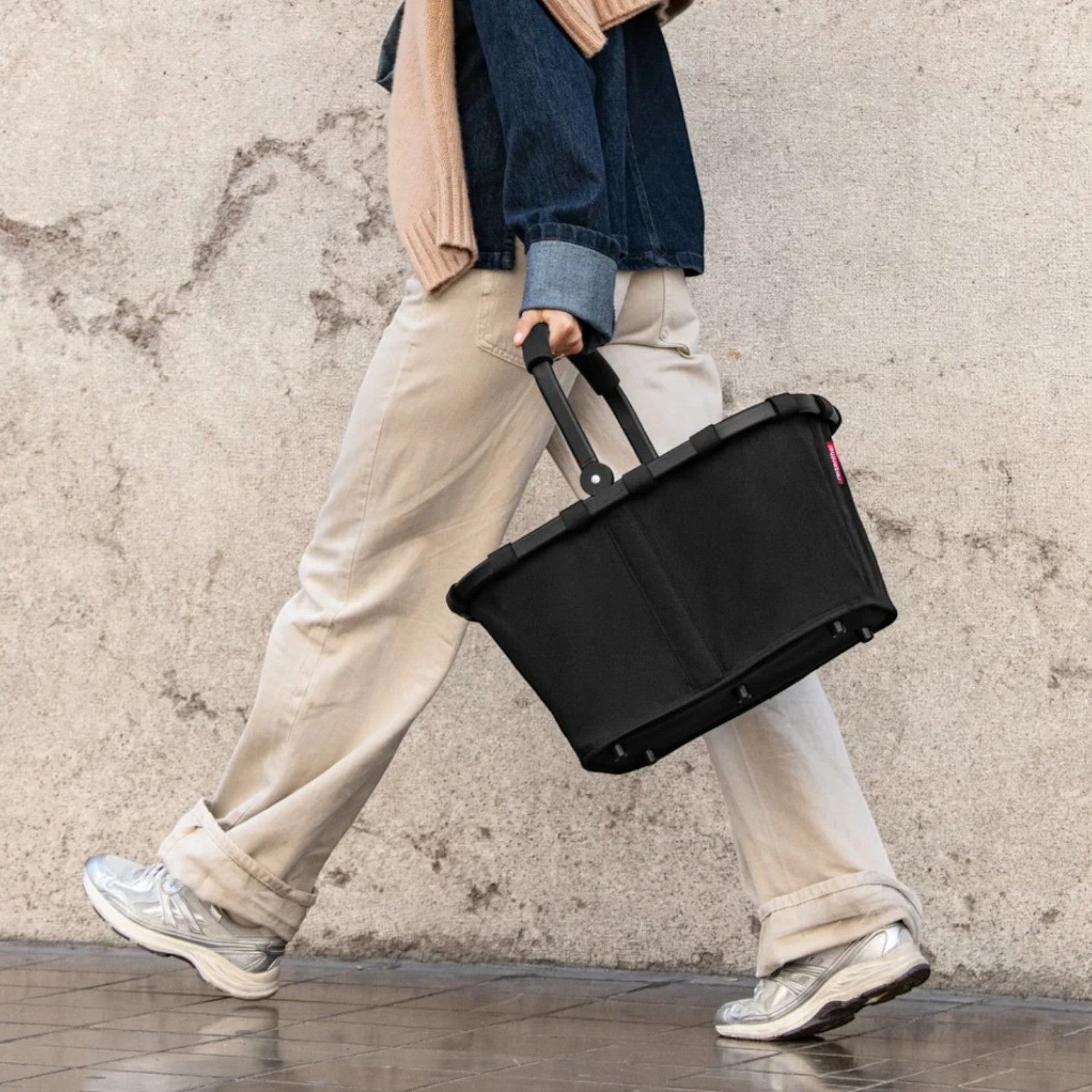 Lieblingstasche Carrybag in black with a sturdy aluminium handle, carried by a woman walking on a city sidewalk.
