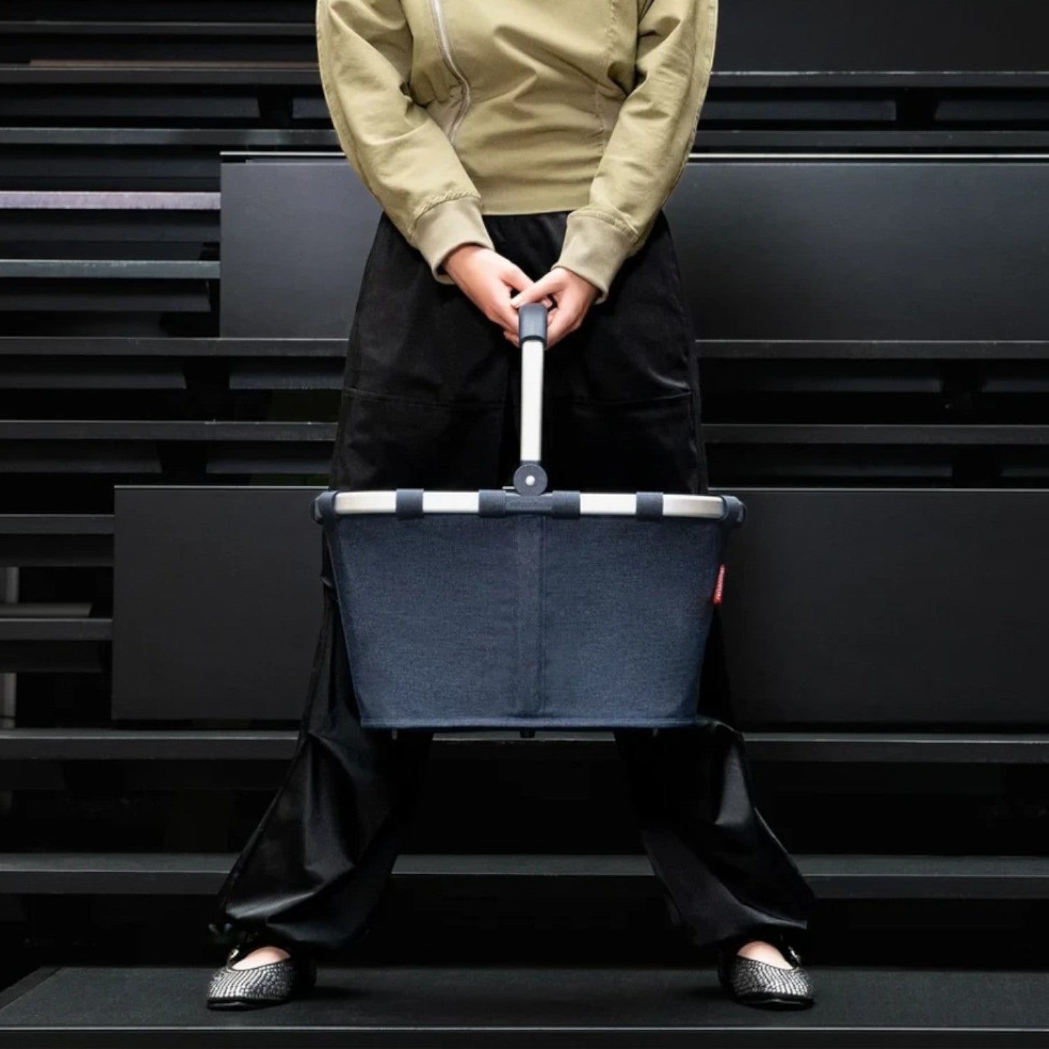 Lieblingstasche Carrybag in dark blue with a sturdy aluminium handle held by a woman on a black staircase