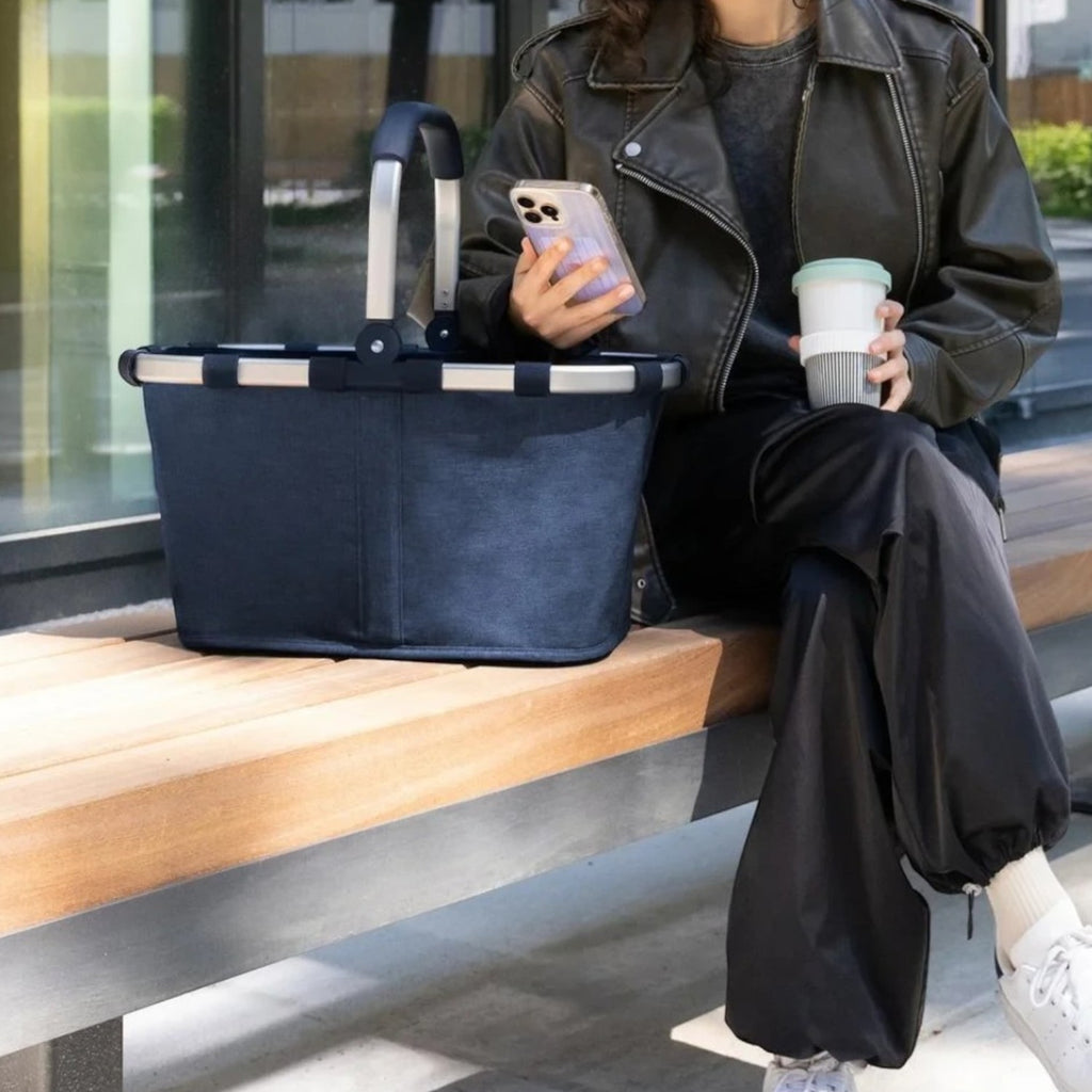 Lieblingstasche Carrybag in navy blue with aluminium handle, sitting on a bench next to a woman in a leather jacket