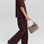 Lieblingstasche Cool Companion Suede S handbag in taupe held by a model wearing a dark burgundy matching set