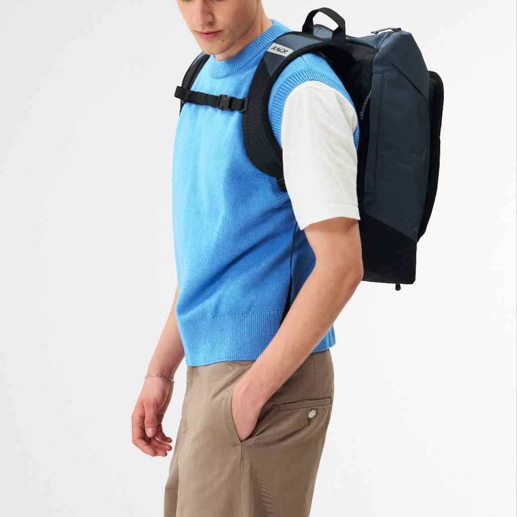A man wearing a Lieblingstasche Day Pack FLX backpack in dark blue, featuring a modern, minimalist design.
