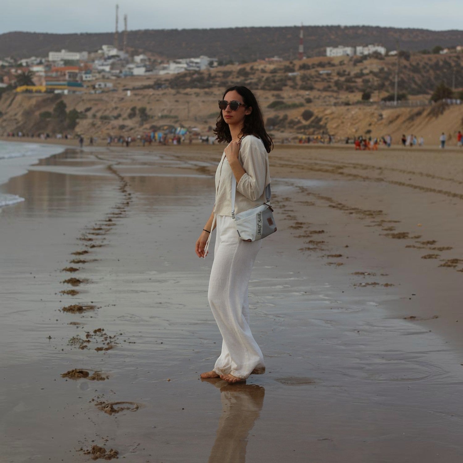 Woman wearing a Lieblingstasche Deern Lütt crossbody bag on a sandy beach at sunset