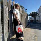 Lieblingstasche Deern Mini canvas tote bag with red letter A detail held by a woman leaning against a wooden fence