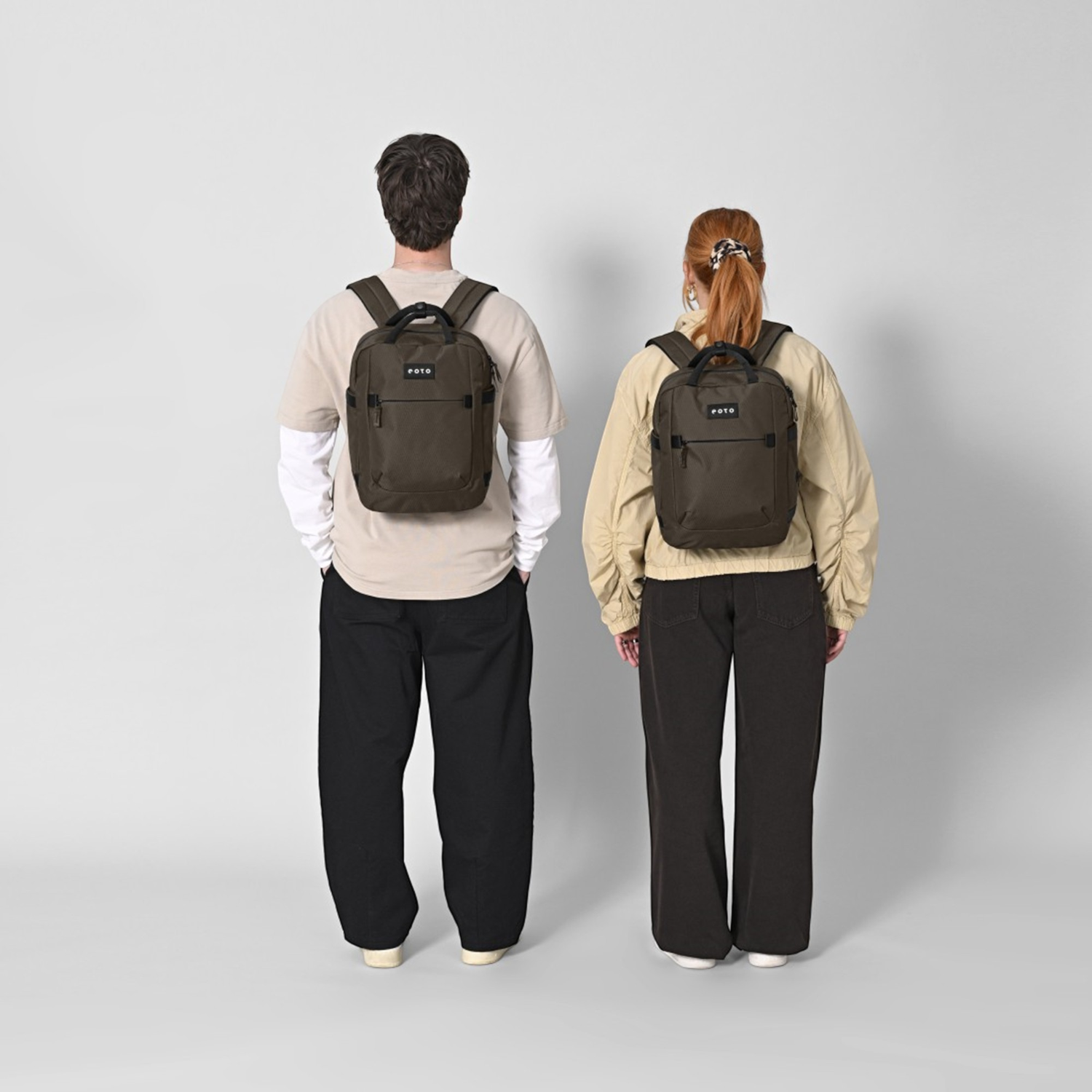 Lieblingstasche eoto Small16 compact daypack in dark brown worn by a man and a woman against a light grey background