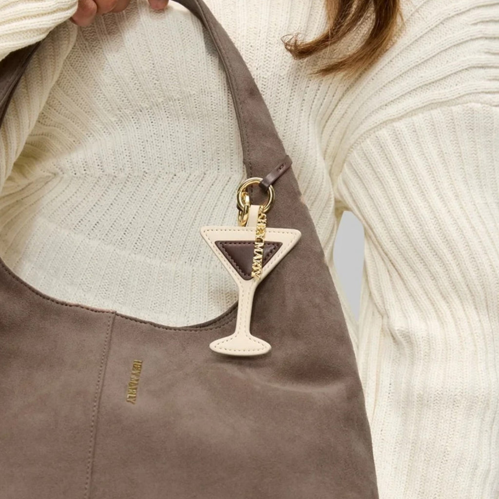 Lieblingstasche Espresso Martini charm hanging from a taupe suede hobo bag held by a person in a cream sweater.