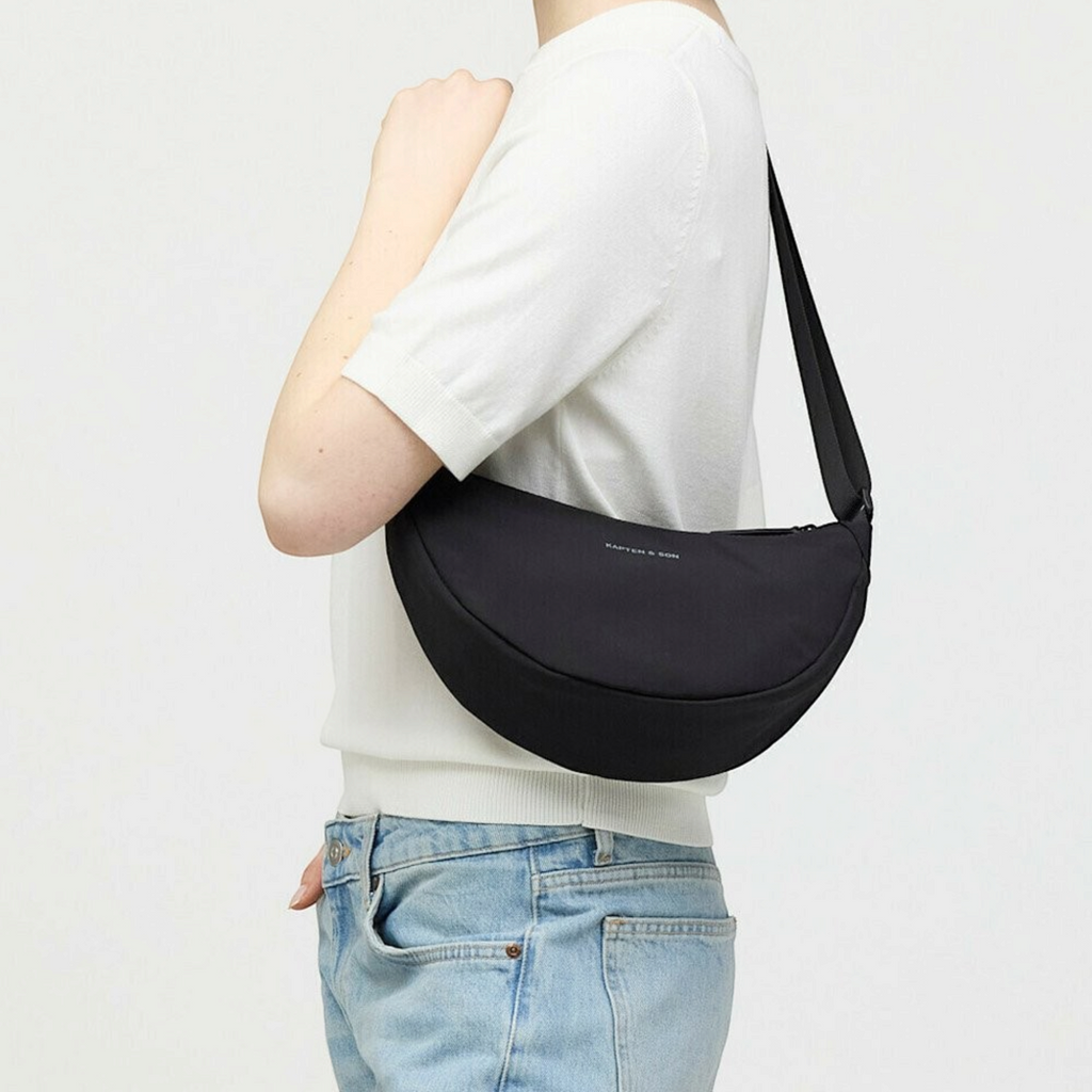 Lieblingstasche Essential Moon Bag in black worn as a shoulder bag by a woman in a white top and jeans