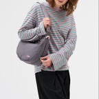 Lieblingstasche grey crescent-shaped sling bag worn over the shoulder by a woman in a striped long-sleeve shirt.
