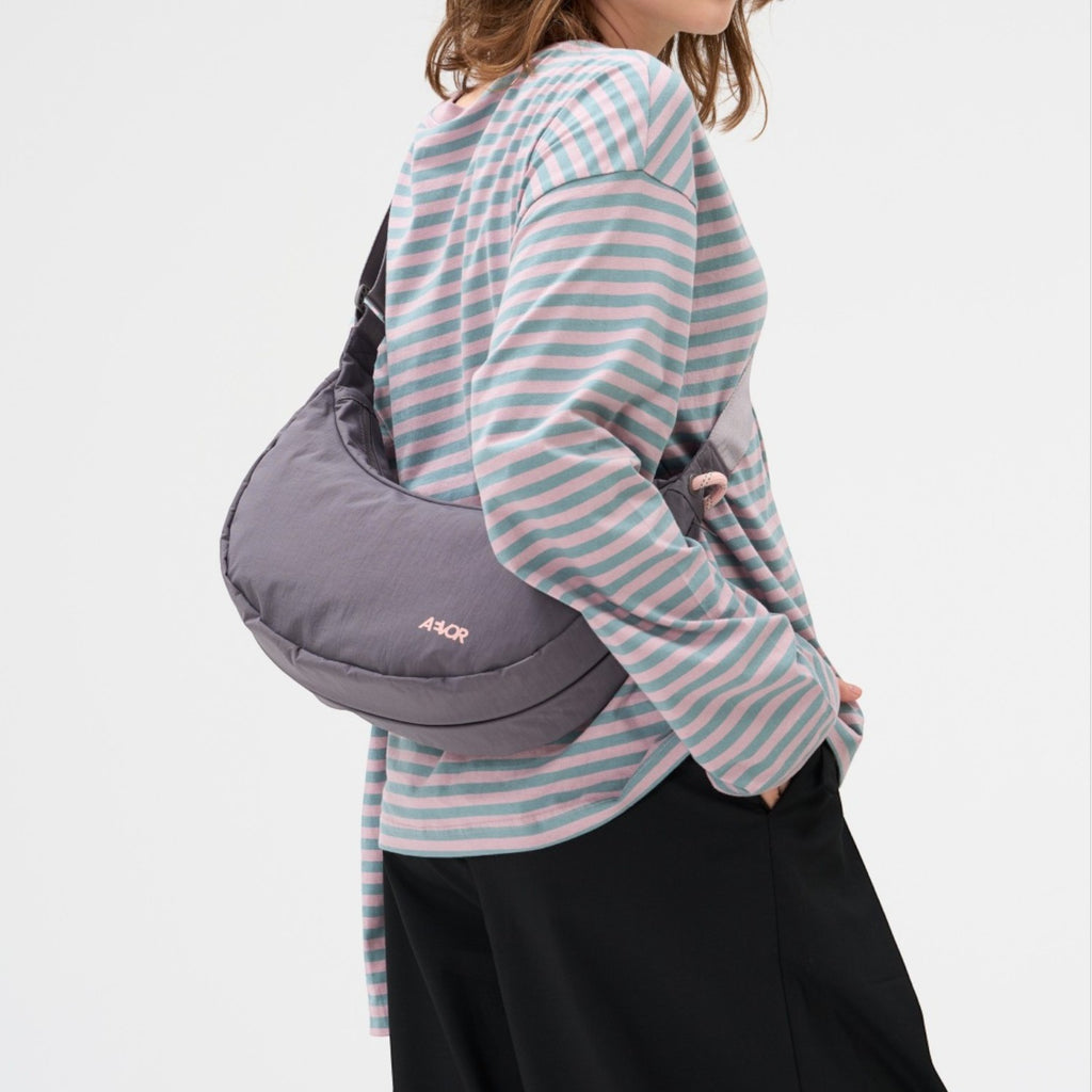 Lieblingstasche grey crescent-shaped sling bag worn over the shoulder by a woman in a striped long-sleeve shirt