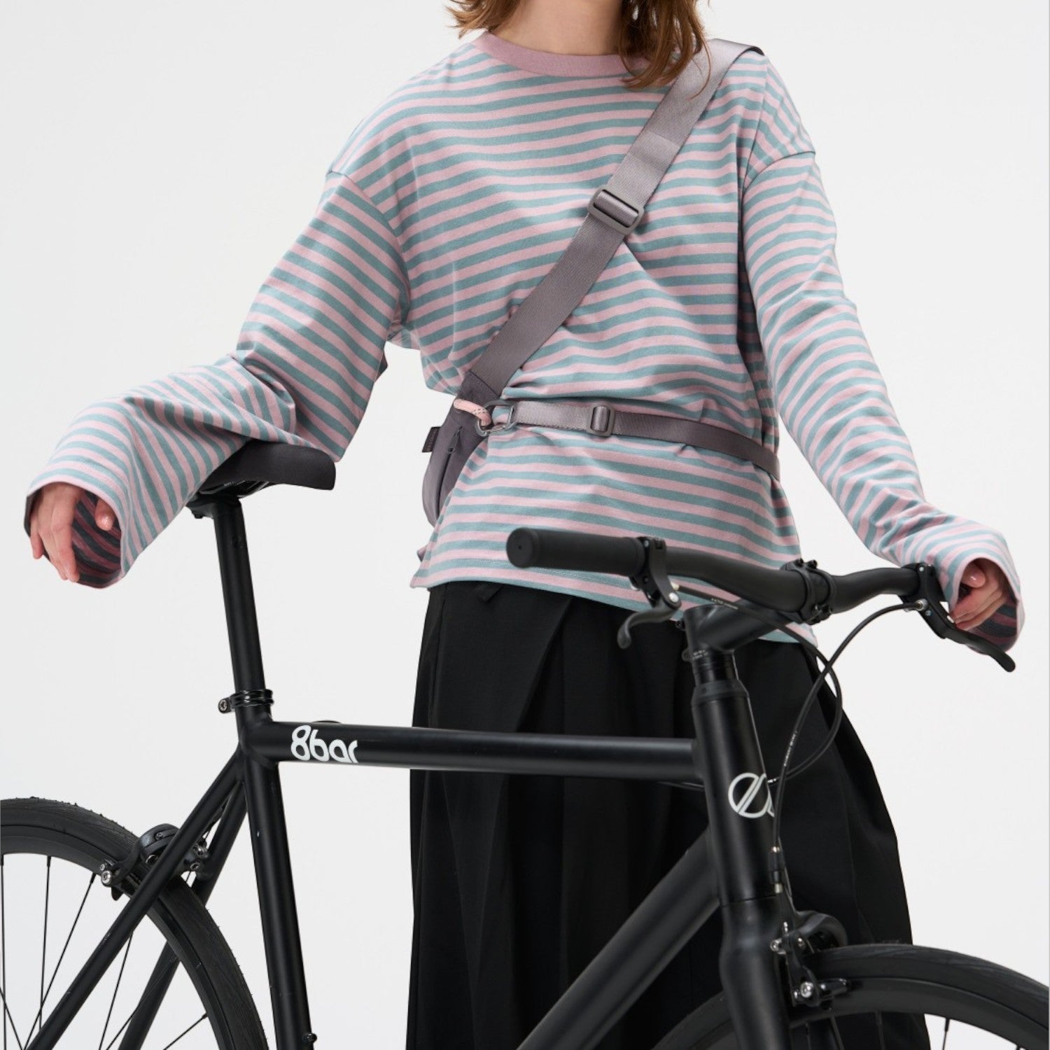Lieblingstasche grey sling bag worn across the chest by a woman in a striped long-sleeve shirt with a black bicycle