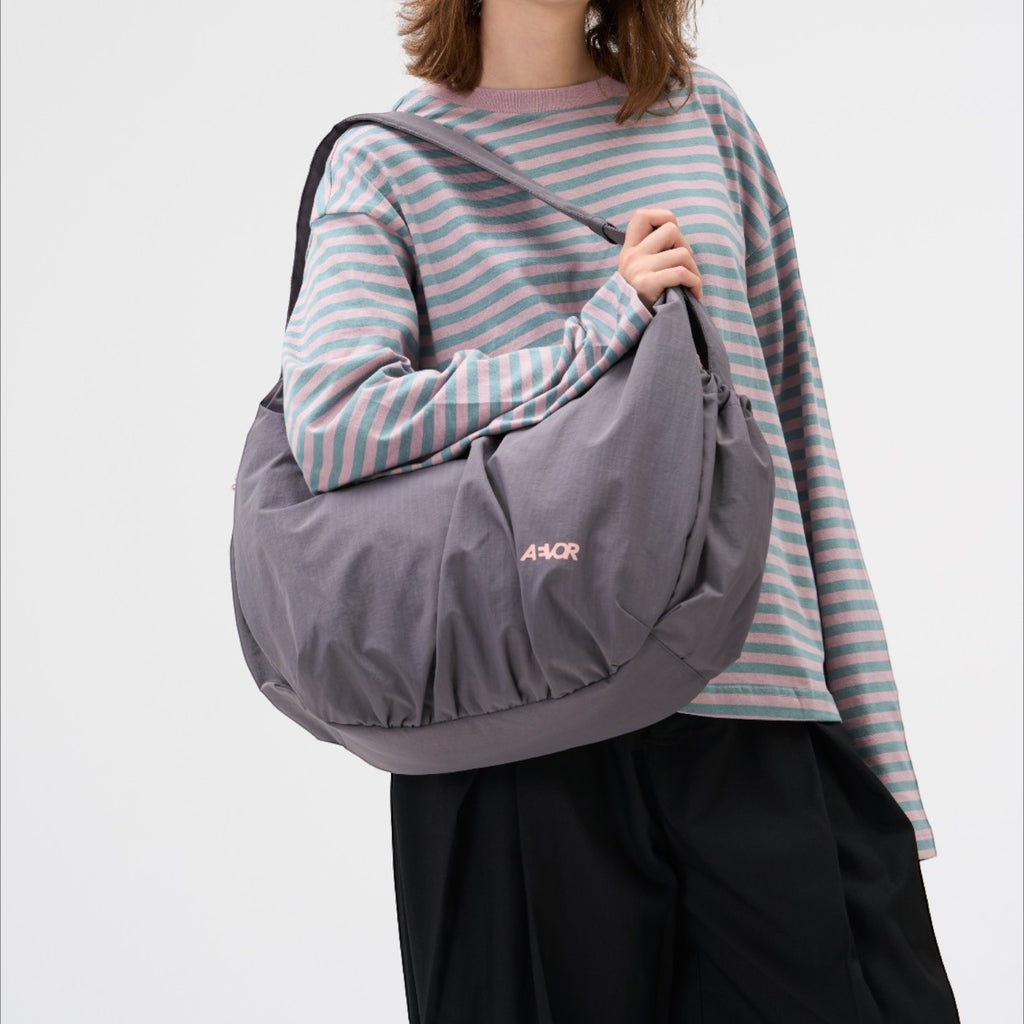 Lieblingstasche slouchy grey shoulder bag with pink logo worn by a model in a striped long-sleeve shirt