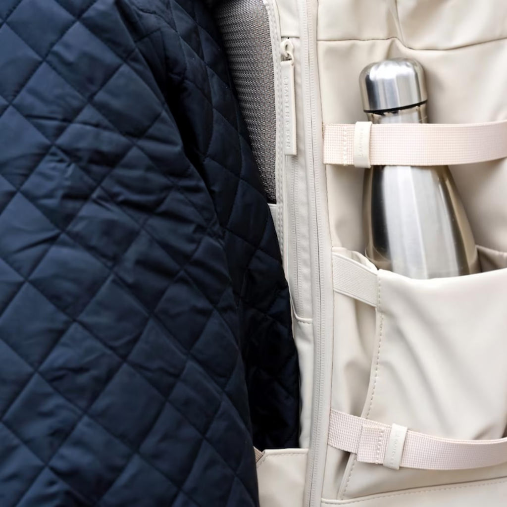 Lieblingstasche Helsinki Pro backpack in beige with a side pocket holding a silver water bottle next to a jacket
