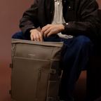 Lieblingstasche Helsinki Pro brown rolltop backpack with side straps and front zip pocket held by a seated man