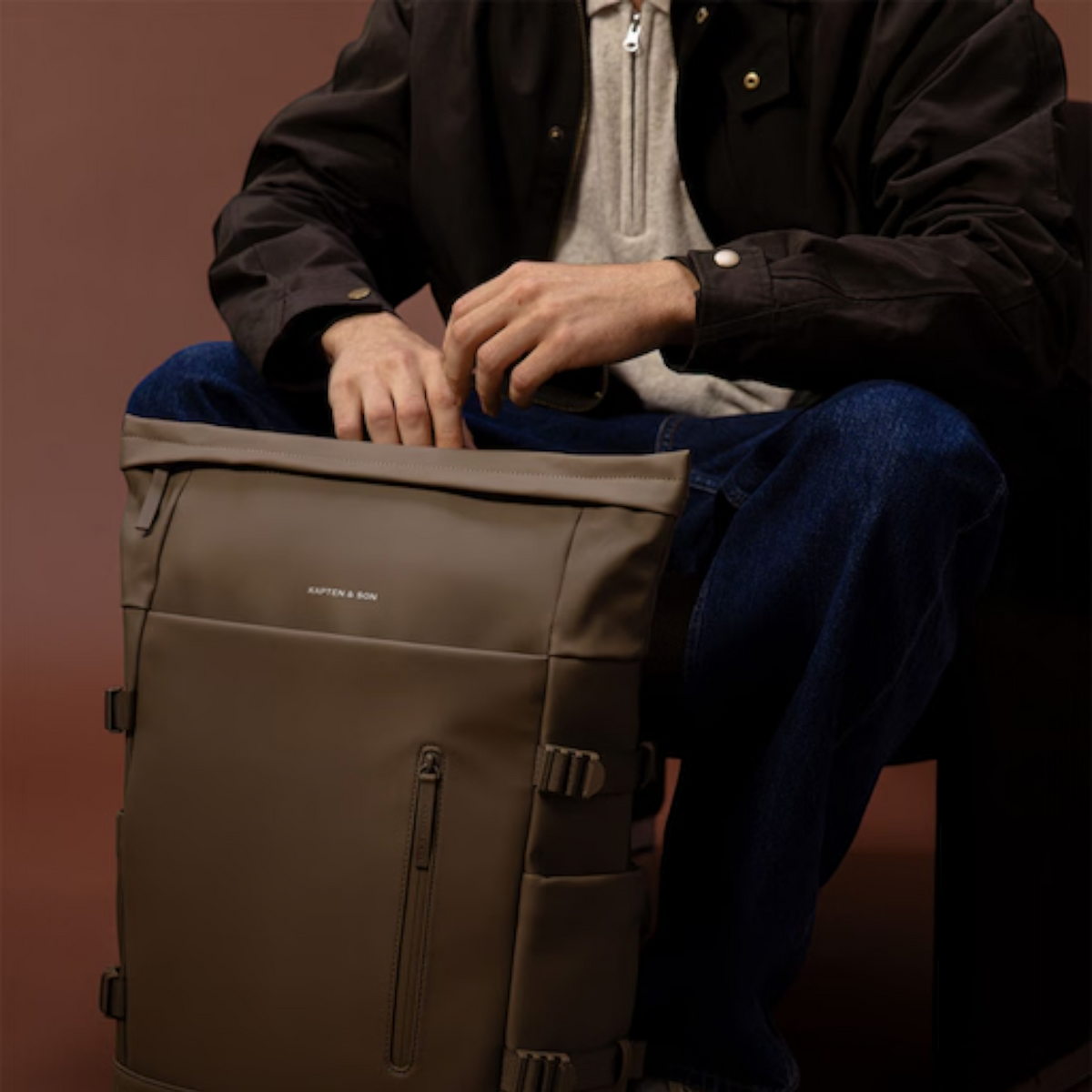 Lieblingstasche Helsinki Pro brown rolltop backpack with side straps and front zip pocket held by a seated man