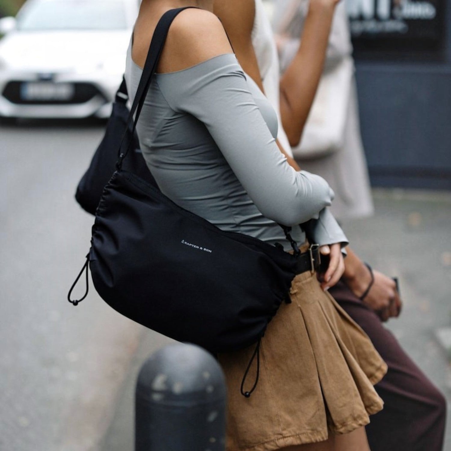 Lieblingstasche Kapten & Son Skara Small black crossbody bag worn by a woman in a grey top and brown skirt