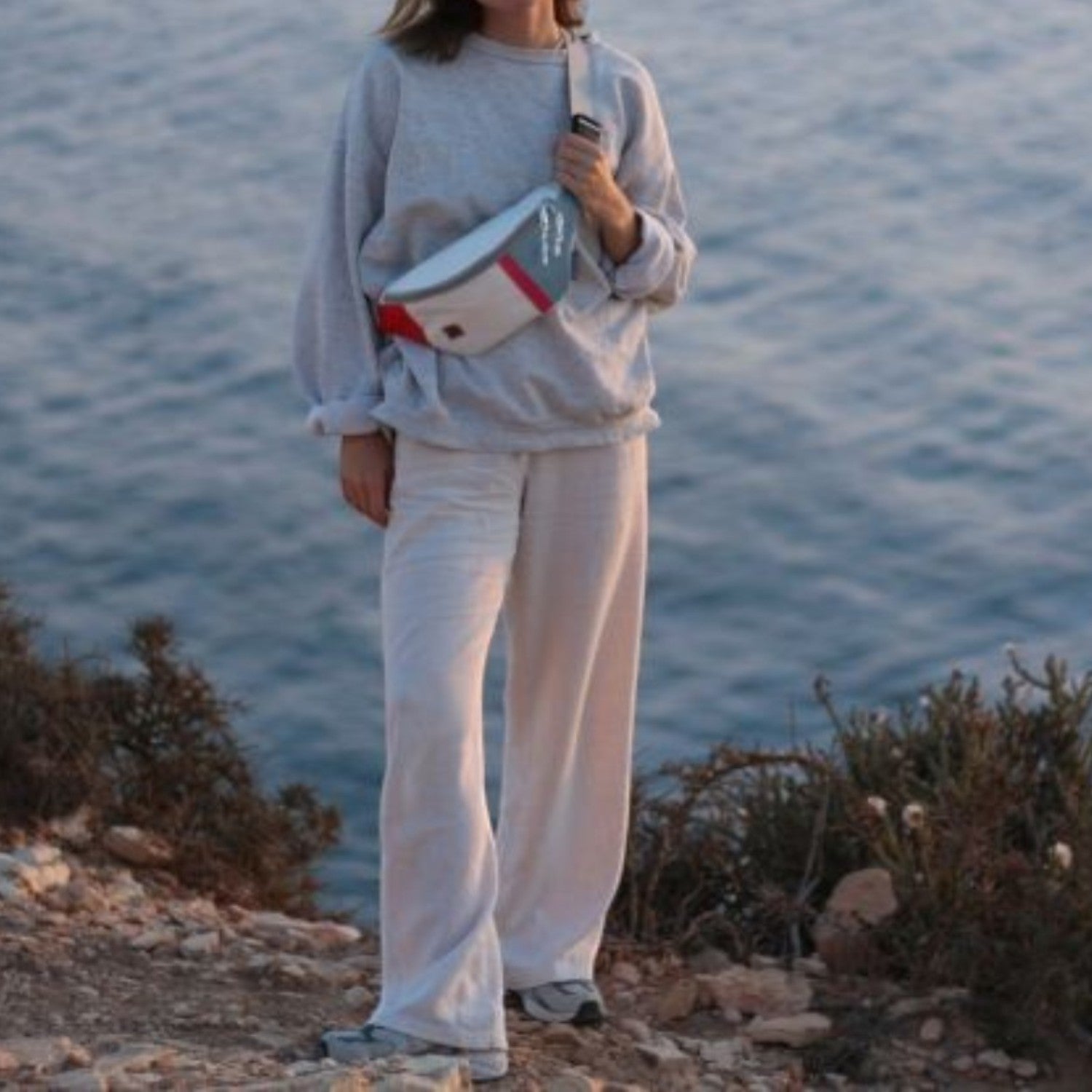 Lieblingstasche Knoten belt bag made from recycled sailcloth with red and grey accents worn by a woman by the sea