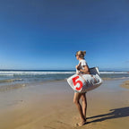 Woman carrying a white Lieblingstasche Kutter XL sailcloth beach bag with a large red number 5 on a sunny beach